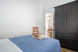 Un dormitorio con cama, una silla de madera, un armario y una puerta que da a otra habitación.