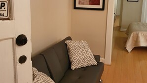 Une pièce avec un canapé gris foncé, des coussins décoratifs à motifs, un tableau abstrait encadré et un plancher en bois.