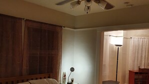 Une chambre à coucher avec un lit, une table de chevet, une lampe sur pied et un ventilateur de plafond.