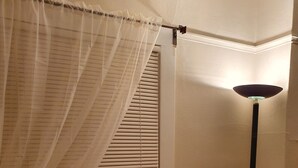 Une pièce avec une fenêtre, un climatiseur, un lampadaire et une chaise noire.
