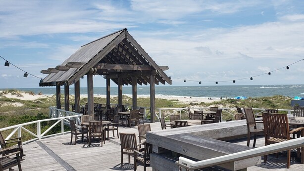 Une terrasse en bois avec des tables et des chaises donnant sur la plage.