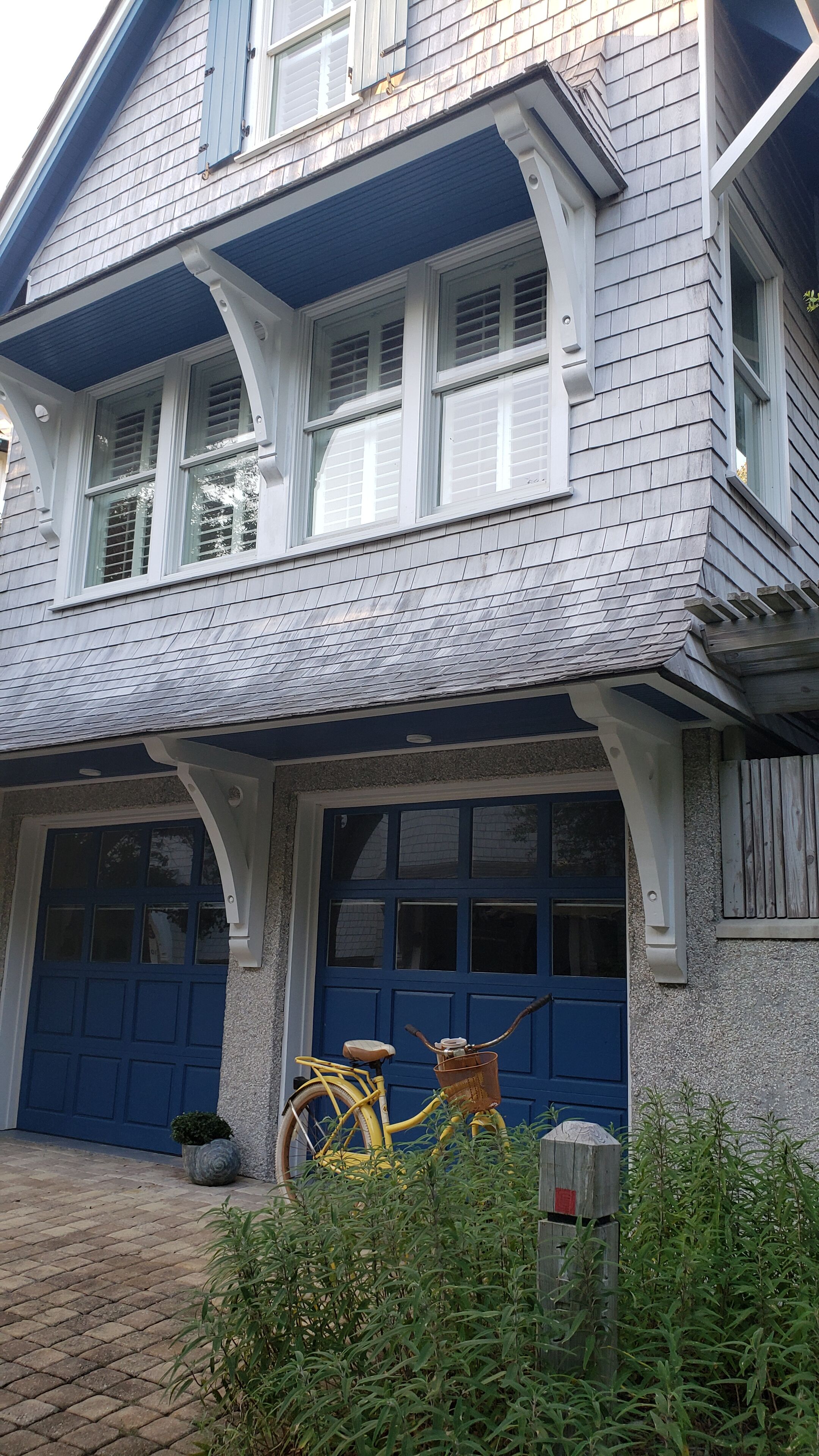 Une maison à deux étages avec une porte de garage bleue, un vélo jaune et un petit jardin.
