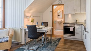 Een moderne keuken met witte kasten, een eethoek met een tafel en stoelen, en een zichtbare klok aan de muur.