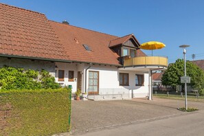 A two-story house with a balcony, a yellow umbrella, and a sign indicating a free parking area.