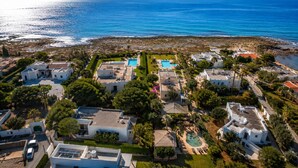 An aerial view of a coastal residential area with houses, a swimming pool, and a clear view of the sea.