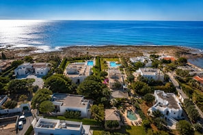 Vista aerea di una zona residenziale costiera con case, una piscina e una limpida vista sul mare.