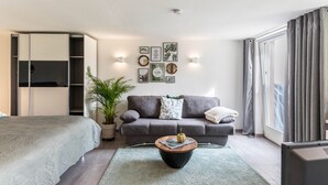 A modern bedroom with a bed, a grey sofa, a coffee table, a potted plant, and wall art. - Schweizer Holiday Apartment – Relaxing Getaway at Lake Constance in Hemmenhofen (Gaienhofen)