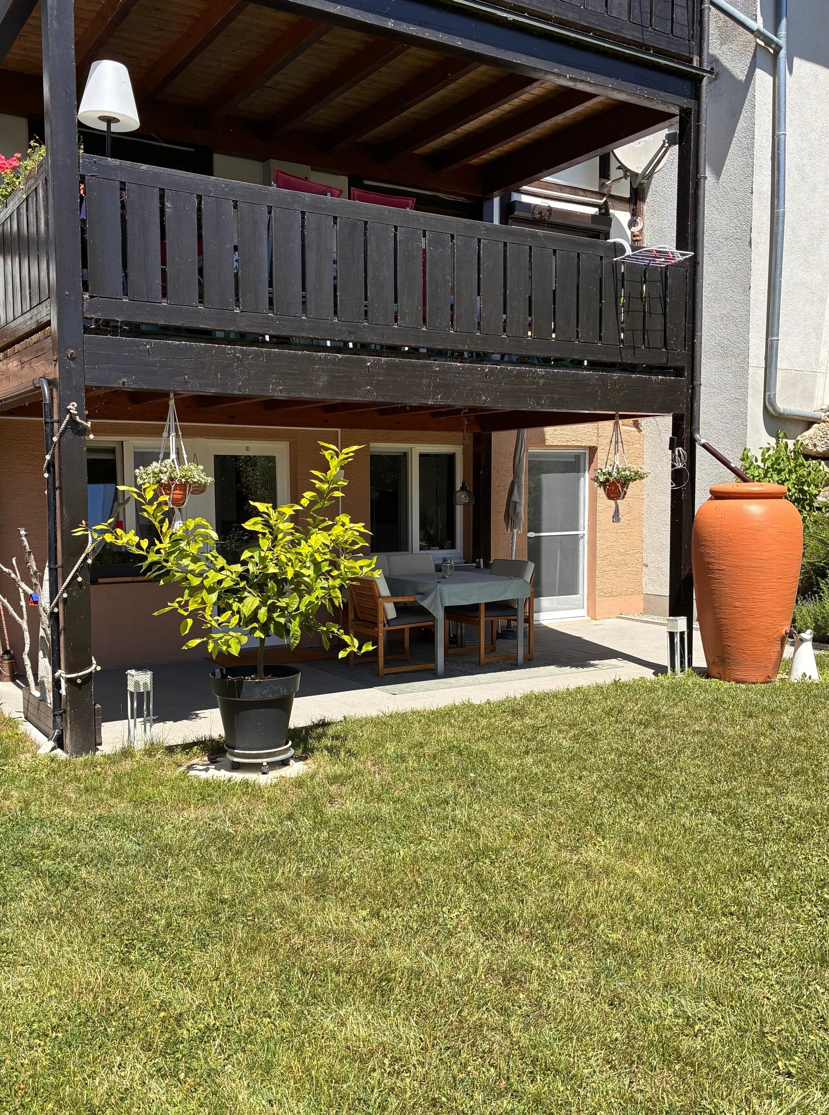 A two-story building with a balcony, a table and chairs outside, and potted plants.
