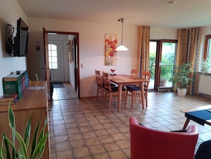 A dining area with a wooden table and chairs, a television on the wall, and a door leading to another room.