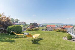 A grassy backyard with two yellow lawn chairs, a neatly trimmed hedge, and a view of houses in the distance.
