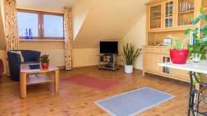 Una sala de estar con sofá, televisor, aparador de madera y plantas en macetas.