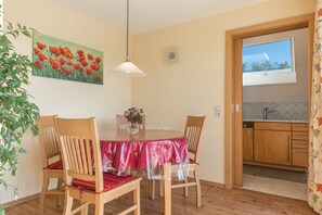 Un comedor con una mesa redonda, sillas, una lámpara colgante, un reloj y una ventana a la cocina.
