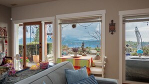 A living room with a sofa, a dining table with a colorful tablecloth, and a view of mountains through large windows.