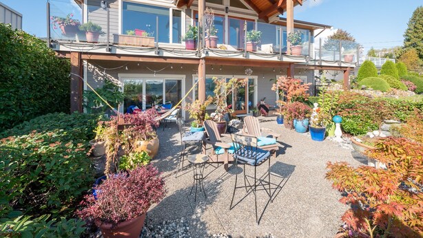 A two-story house with a covered patio area, multiple potted plants, and outdoor furniture.