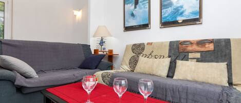 A living room with a grey sofa, a red table with three wine glasses, and two framed pictures on the wall.