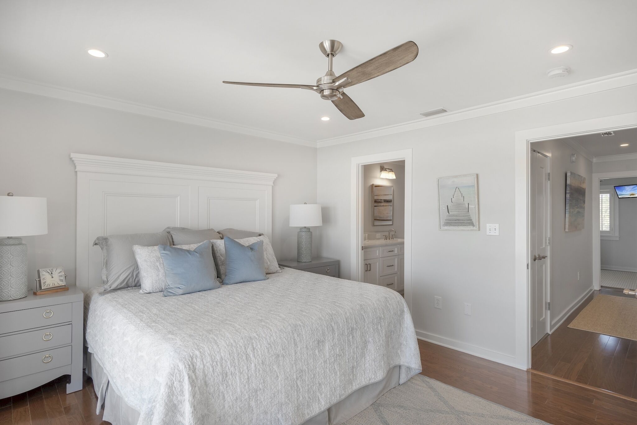 A bedroom with a bed, nightstands, a ceiling fan, a dresser, and a door leading to another room.