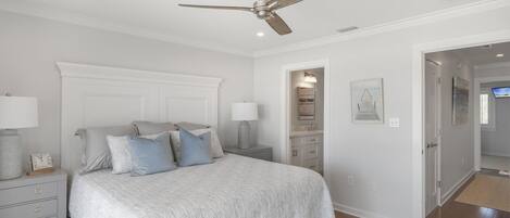 A bedroom with a bed, nightstands, a ceiling fan, a dresser, and a door leading to another room.