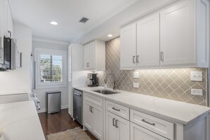 Una cocina moderna con armarios blancos, lavavajillas integrado y una ventana con persianas.