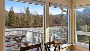 Une terrasse dotée de bancs et de chaises en bois, offrant une vue sur une rivière et des montagnes boisées.