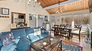 Un vaste espace de vie comprenant un canapé bleu, une table à manger en bois et des chaises, une cuisine à l’arrière-plan et un balcon doté d’une balustrade.