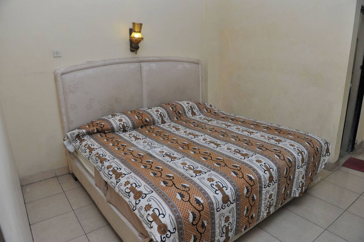 A bed with a patterned bedspread, a wall-mounted light fixture, and a tiled floor.