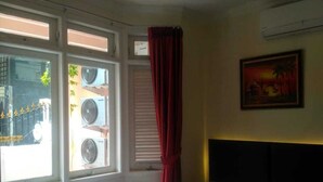 A bedroom with a bed, a window with blinds, an air conditioning unit, and a painting on the wall. - Katalia Tomang (Jakarta)
