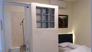 A small, compact room with a shower, toilet, and a bed with a headboard. - Katalia Tomang (Jakarta)