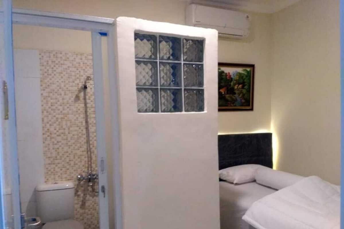 Habitación pequeña y funcional con ducha, inodoro y cama con cabecera.
