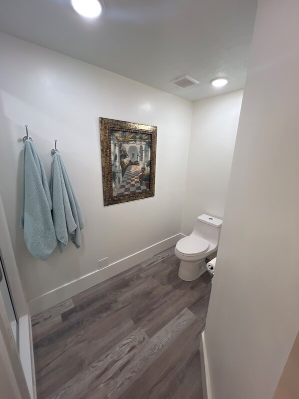 A bathroom with a white toilet, a wooden floor, and a framed artwork on the wall. - Lake front property (Saratoga Springs)