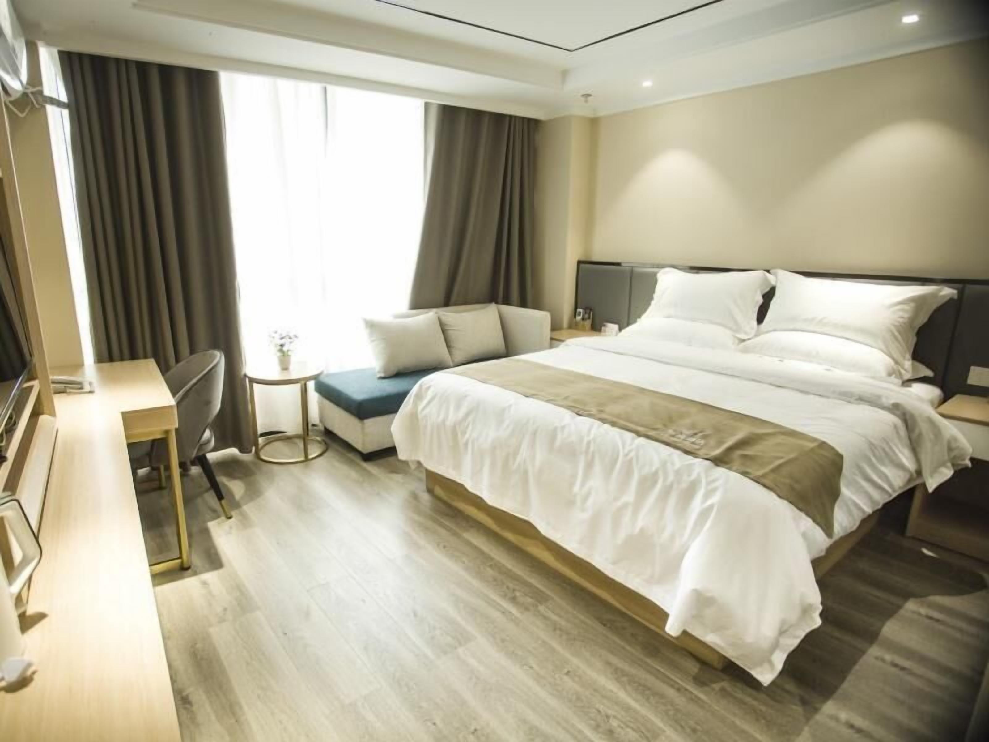 Une chambre d’hôtel avec un lit, un bureau, une chaise, une petite table et une fenêtre avec des rideaux.