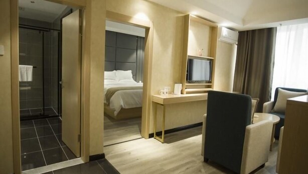 A hotel room with a bed, a desk, a chair, a TV, and a shower area.