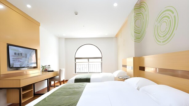 Ein Hotelzimmer mit einem großen Bett, einem Schreibtisch mit Fernseher, einem Fenster mit Aussicht und einem grünen Teppich.