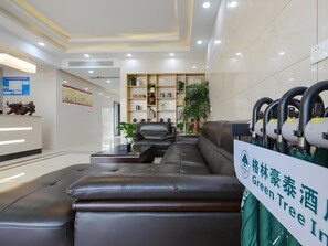 A reception area with a black leather sofa, a reception desk, and a sign indicating a Green Tree Inn. - Greentree Inn Jiaxin Puyuan Kaixuan Road (Jiaxing)