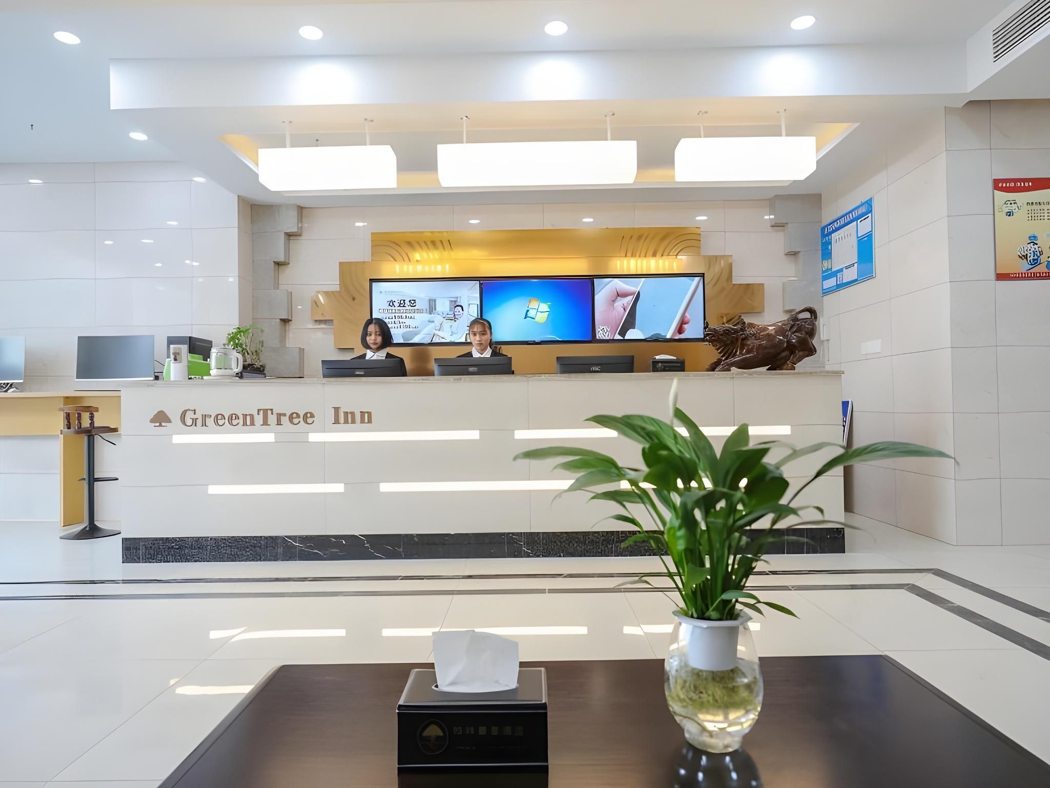 A reception desk with a sign for GreenTree Inn, multiple monitors, a statue, and a plant in a vase.