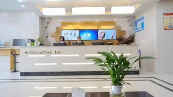 A reception desk with a sign for GreenTree Inn, multiple monitors, a statue, and a plant in a vase.
