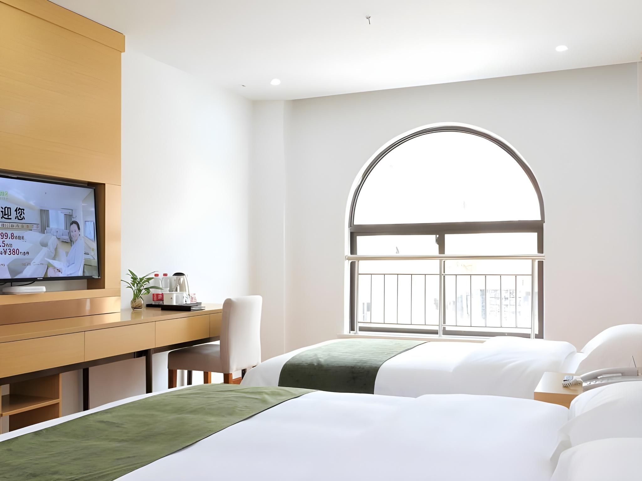 A hotel room with a bed, a desk, a television, and a large arched window.