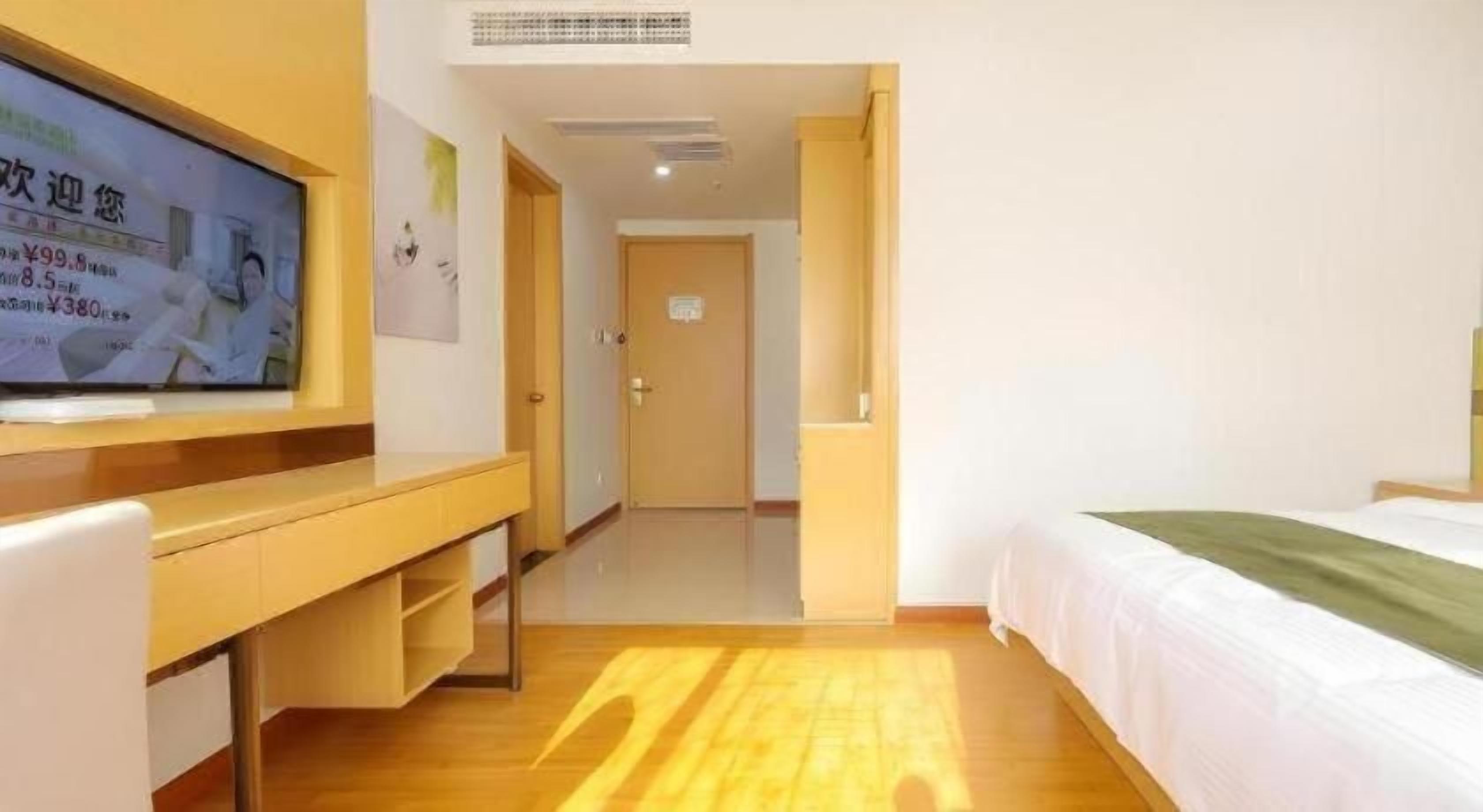 A hotel room with a bed, a desk, a television, and a door leading to another room.