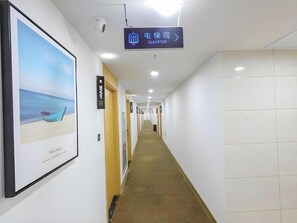 A hotel corridor with a sign indicating an elevator direction, a framed picture on the wall, and a carpeted floor. - Greentree Inn Jiaxin Puyuan Kaixuan Road (Jiaxing)