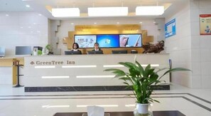 A reception desk with a digital screen displaying images, a sign for GreenTree Inn, and a potted plant in the foreground. - Greentree Inn Jiaxin Puyuan Kaixuan Road (Jiaxing)