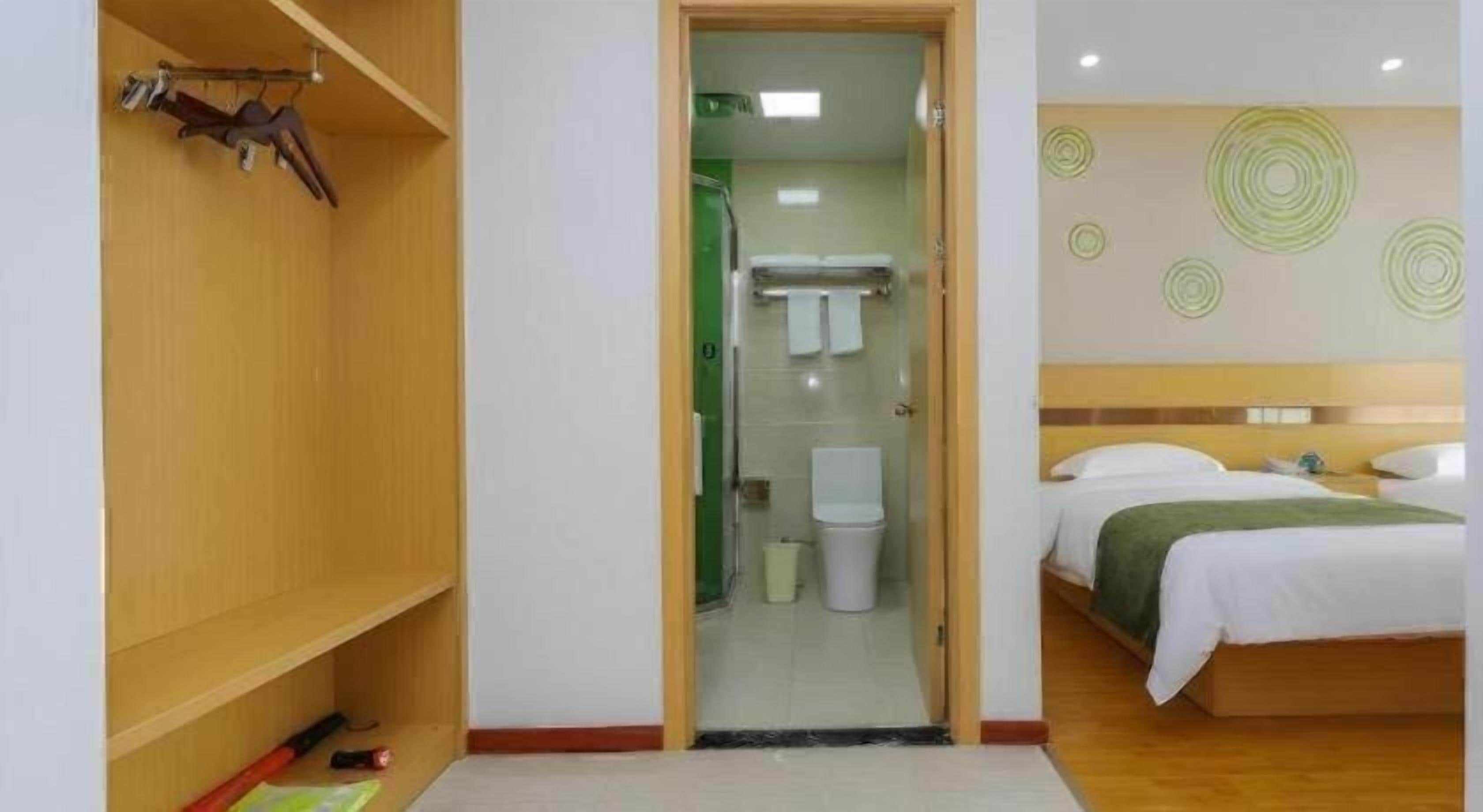 A hotel room with a wooden wardrobe, a bed with white bedding, a bathroom with a toilet and sink, and a shower area.
