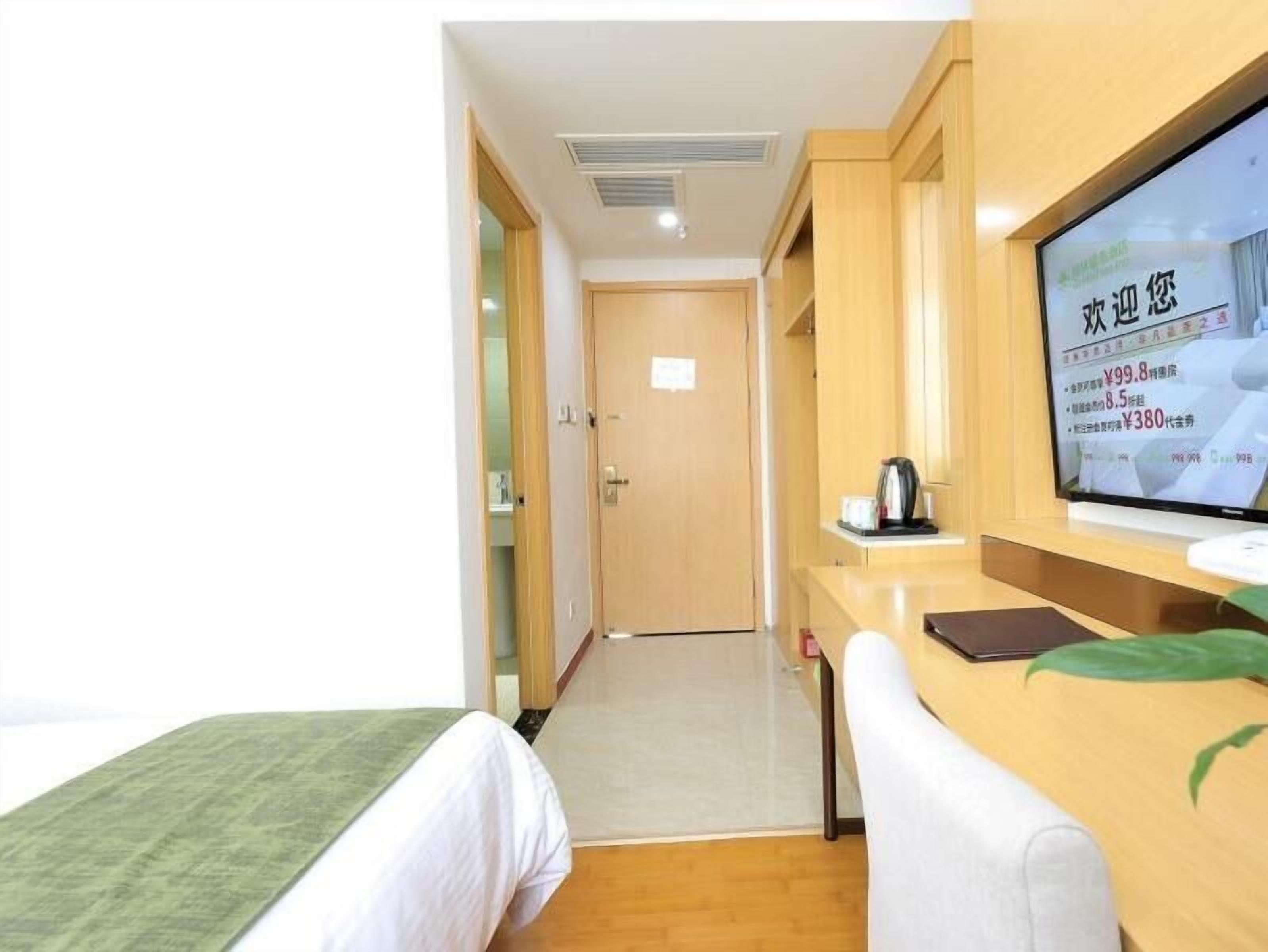 Una camera d'albergo con un letto, una scrivania con un computer e un televisore che mostra un menu.