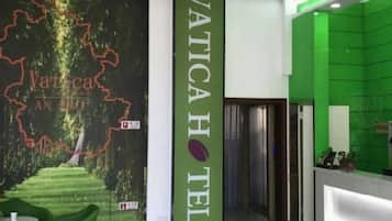 A hotel reception area with a green reception desk, a chandelier, and a wall with a map and the hotel name.