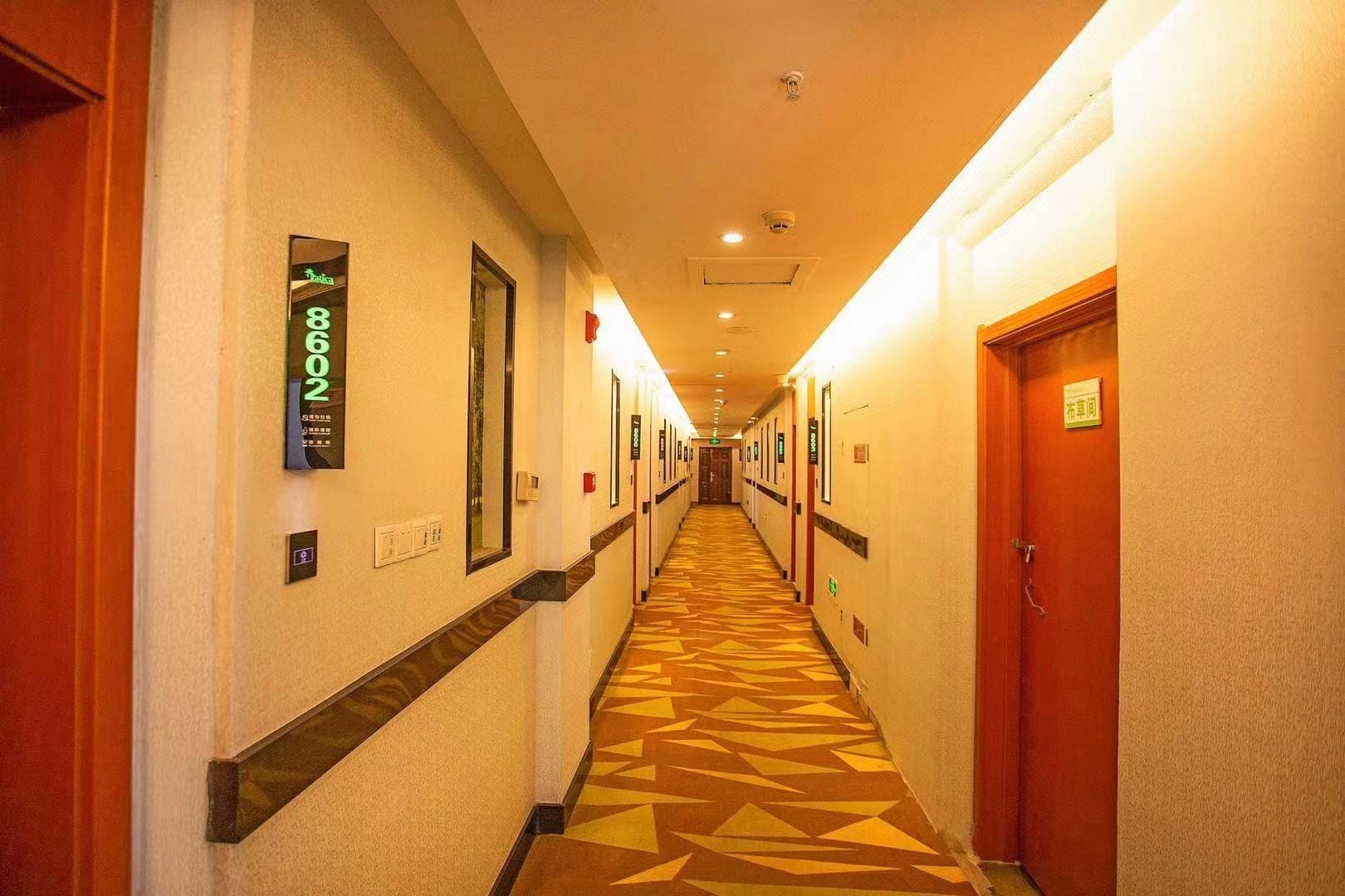A hotel hallway with numbered doors, a patterned carpet, and a long corridor.