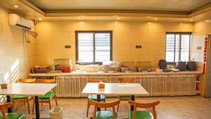 A dining area with tables and chairs, a buffet setup, and a kitchen area with pots and pans. - Vatica Jieshou City New Passenger Transport Center Hotel (Fuyang)