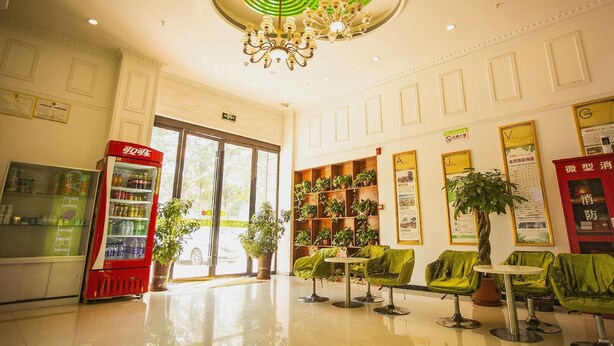 Um saguão com máquina de vendas, cadeiras verdes, um candelabro e uma planta.