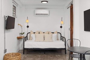 A small, well-lit room with a bed, bedside table, lamp, and a television.