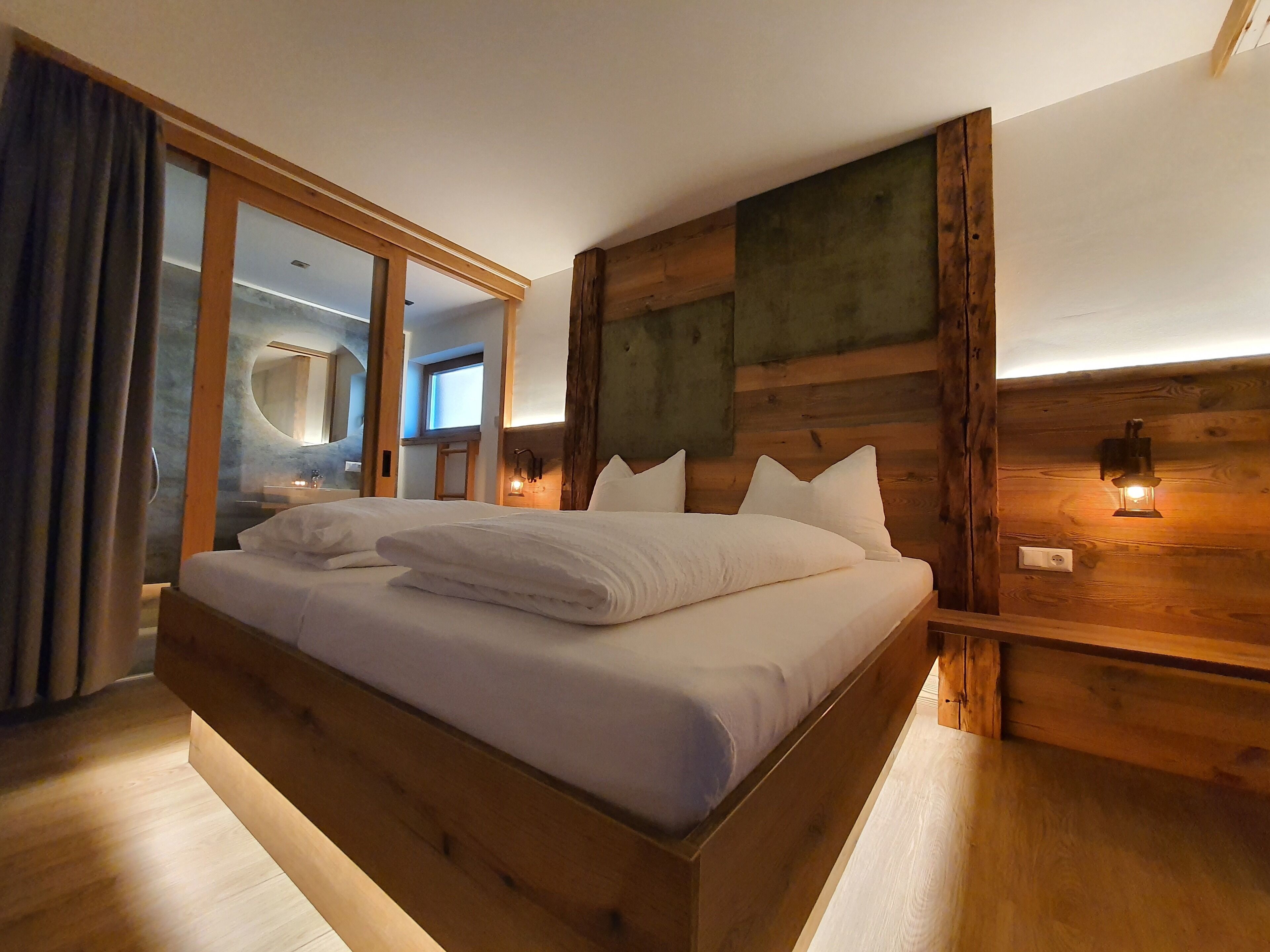 A wooden-framed bed with white linens in a room with wooden walls and a large mirror.