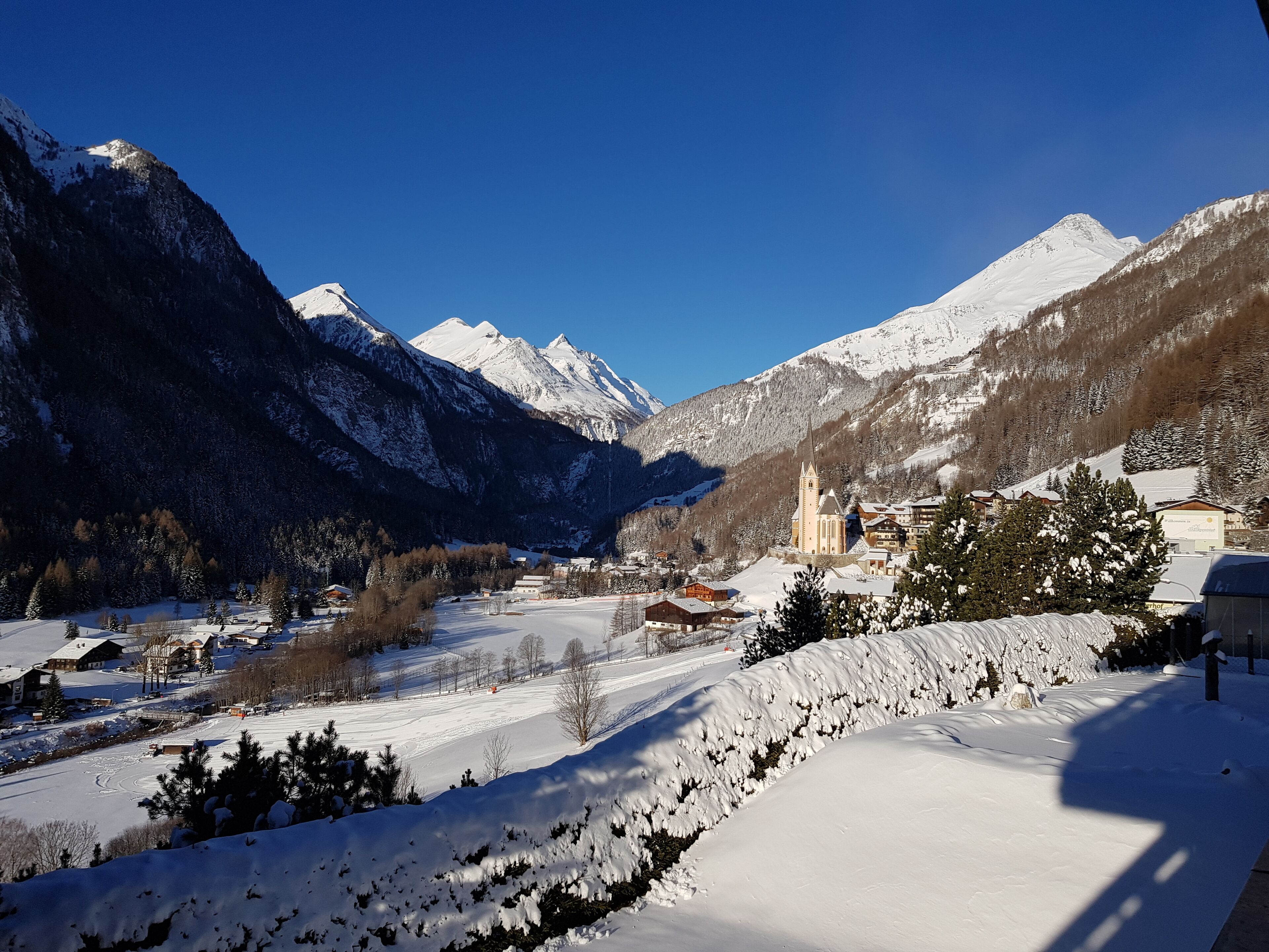 Un paysage montagneux enneigé, avec une église et des bâtiments dans la vallée.