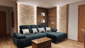 A modern living room with a sectional sofa, wooden walls, and a wooden floor.