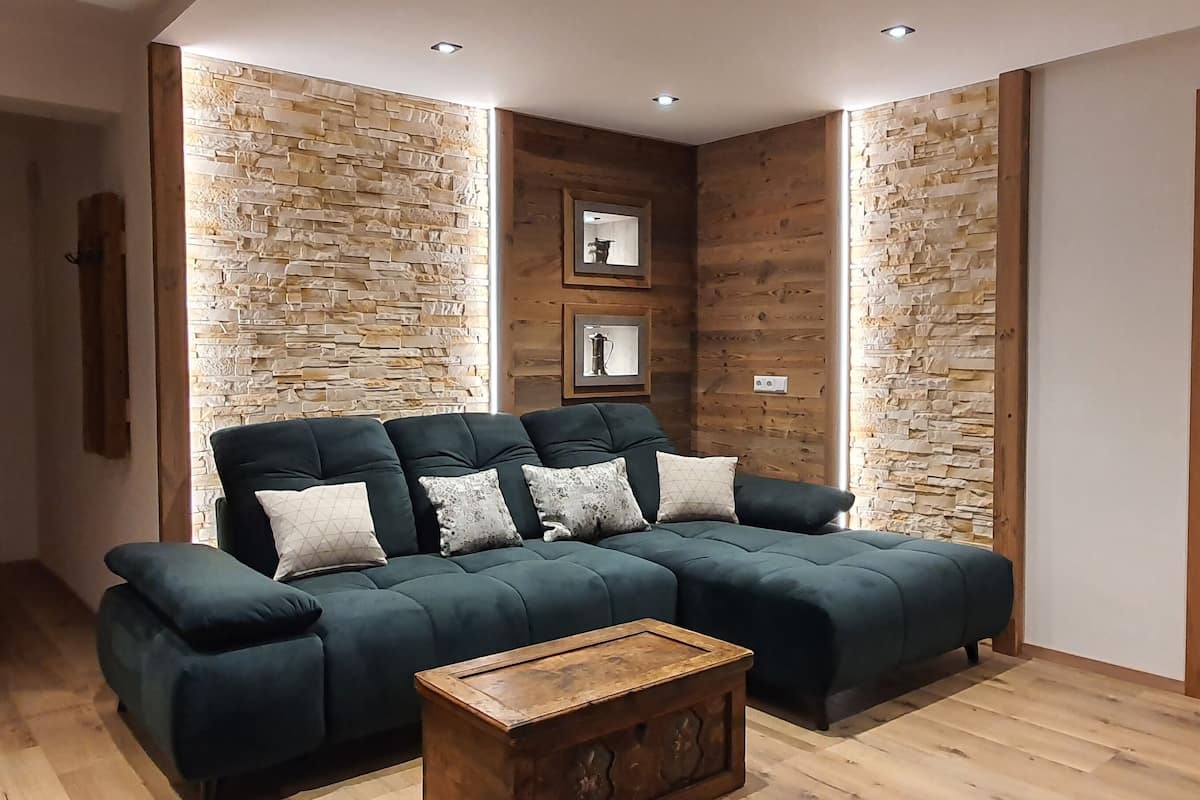 A modern living room with a sectional sofa, wooden walls, and a wooden floor.